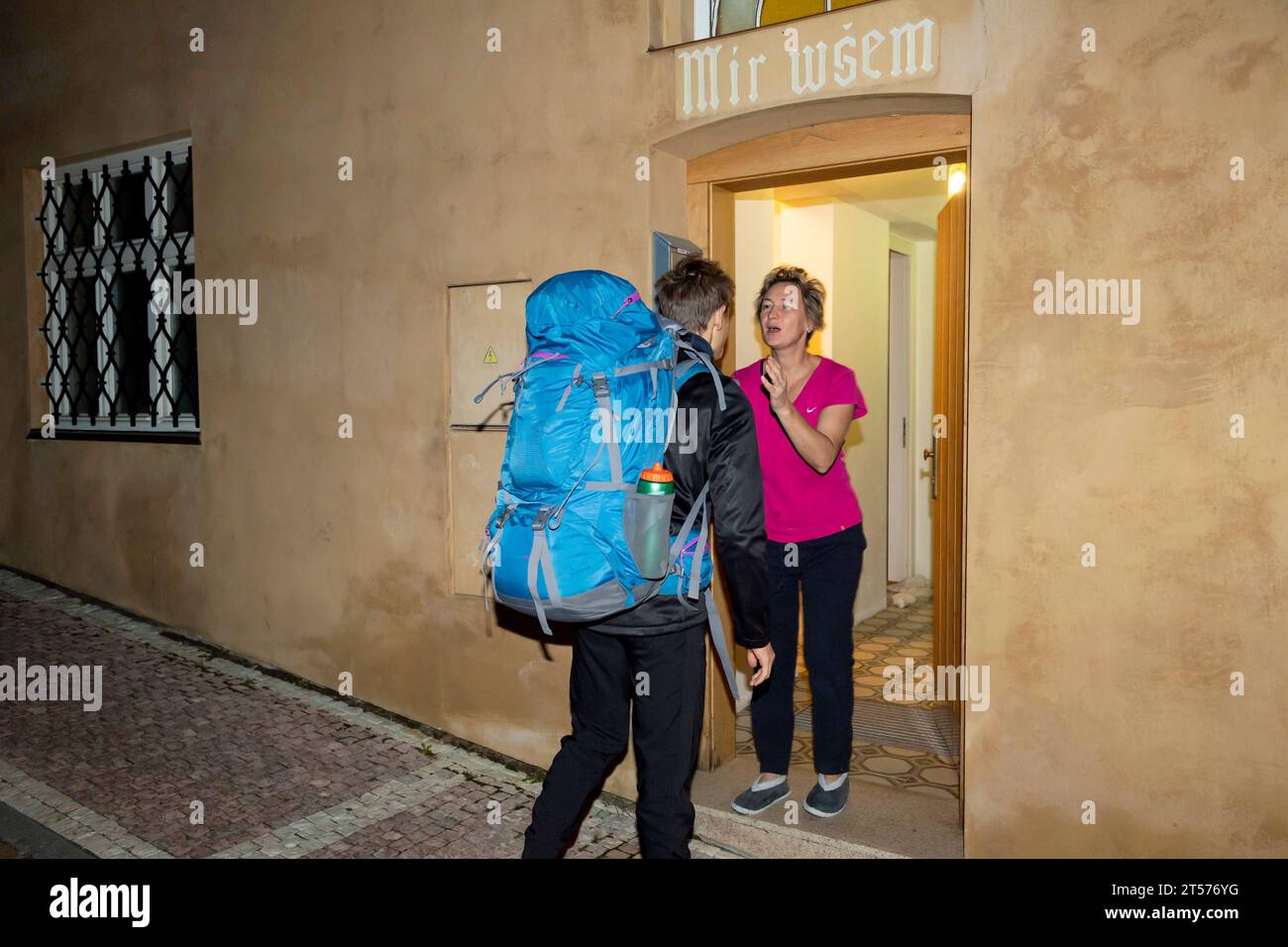 madre alla porta baciando figlio - adolescente con zaino che parte dalla casa di famiglia durante il viaggio Foto Stock