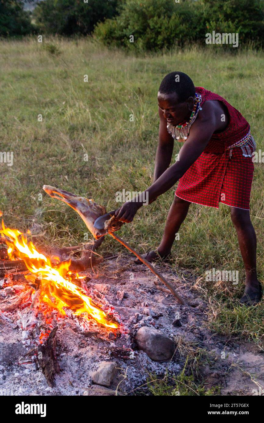 MASAI MARA, KENYA - 20 FEBBRAIO 2020: Uomo Masai che tosta una gamba di capra, Kenya Foto Stock