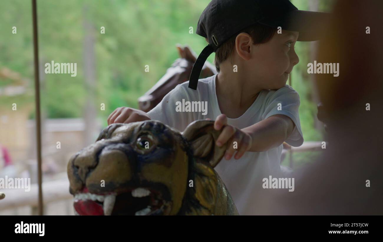 Un bambino felice che cavalca la giostra al parco, un bambino che si gode una giornata d'estate seduto sulla tigre in giostra in movimento Foto Stock
