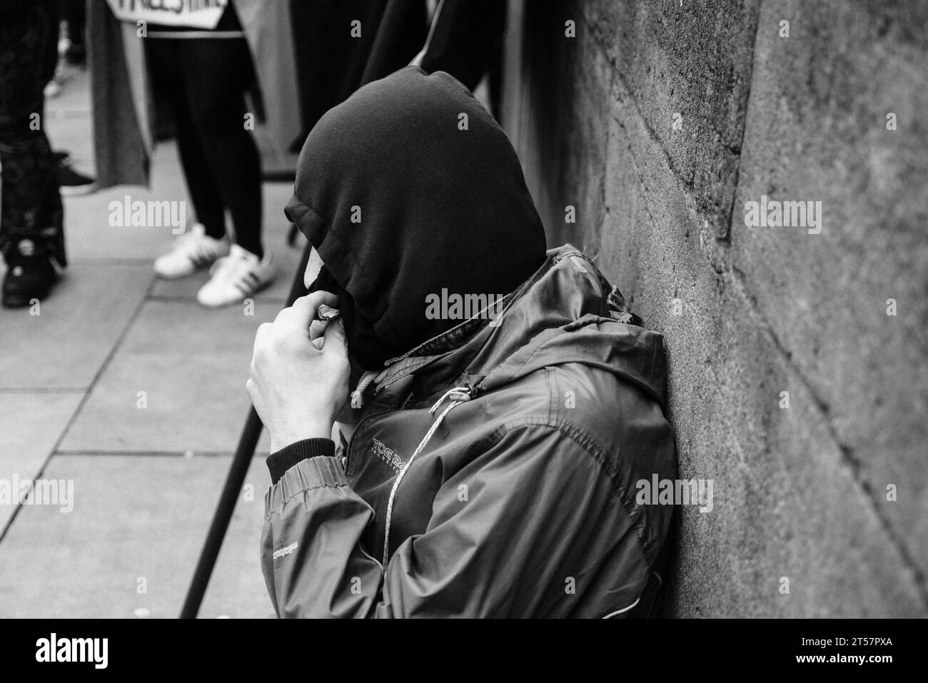 L'uomo con cappuccio lecca la sigaretta arrotolata mentre si appoggia al Grey's Monument alla marcia per il cessate il fuoco di Gaza. Newcastle upon Tyne, Inghilterra, Regno Unito - ottobre 28 2023. Foto Stock