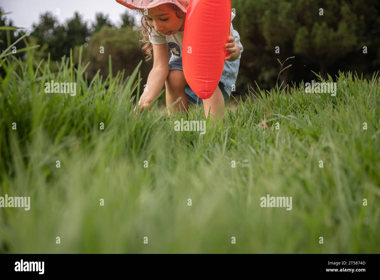 Concetto di infanzia felice, esplorare il mondo intorno a te. Adorabile ragazza scalza che gioca sull'erba in un parco durante il giorno e tiene una mongolfiera. Foto Stock