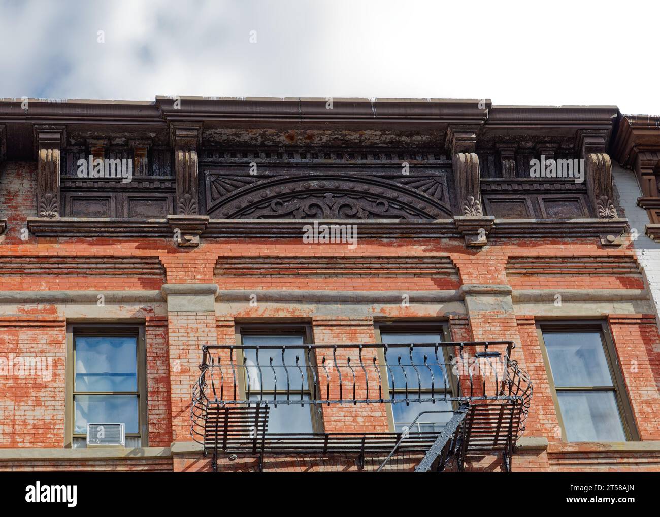 Una cornice metallica dipinta e stampata punteggia la linea del tetto di 523 East 83rd Street; la vernice sta sbiadendo dalla facciata sottostante. Foto Stock