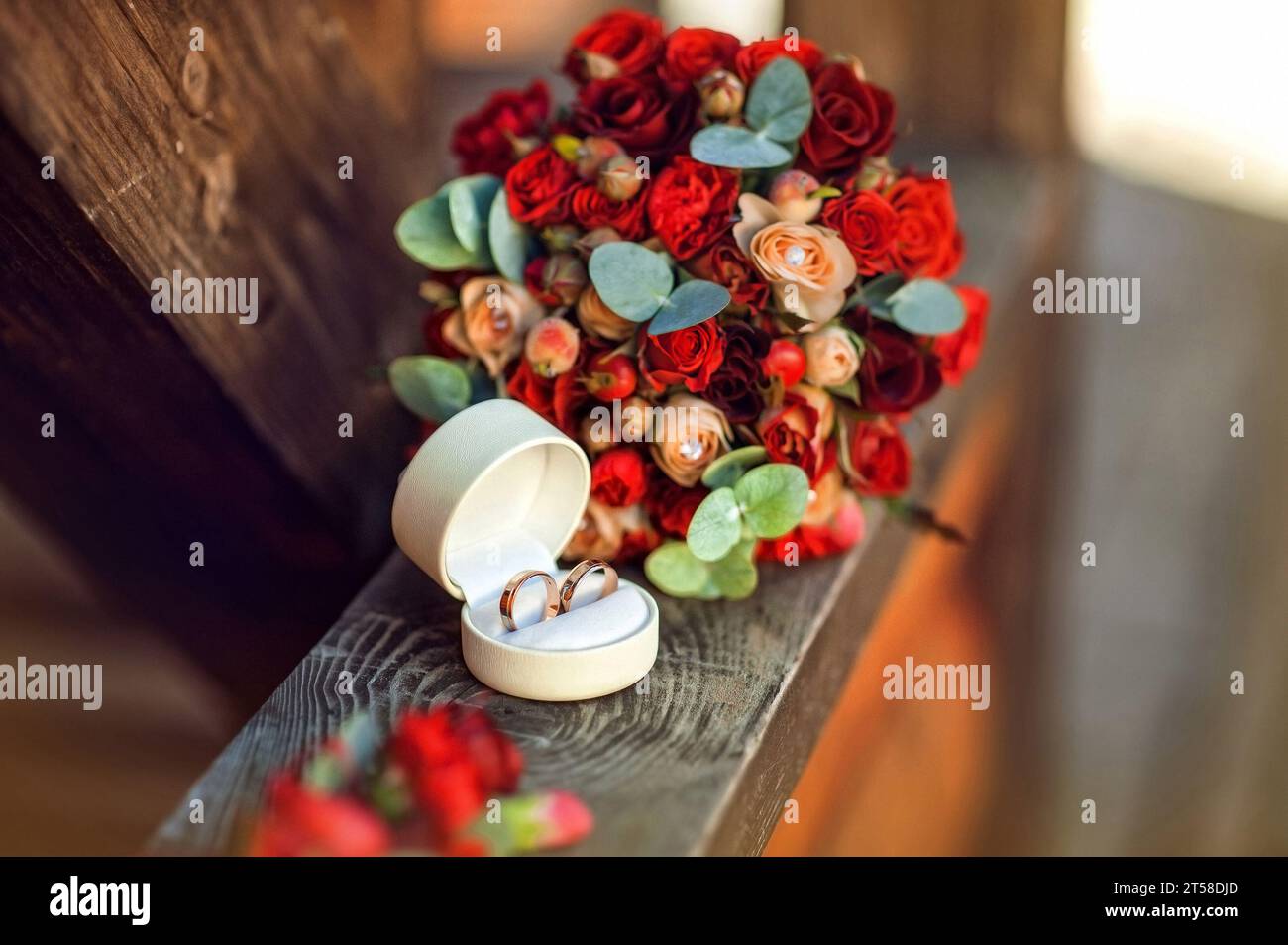 Fedi nuziali vicino al bouquet rosso con rose su sfondo di legno. Accessori nuziali. Il concetto di matrimonio in uno stile etnico nella natura Foto Stock