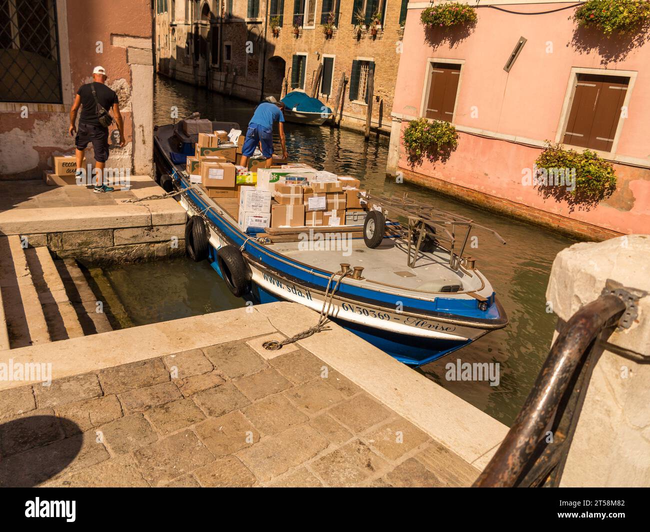 Consegna dei pacchi in barca sui canali di Venezia in Italia. Un addetto alla consegna preleva un pacchetto per consegnarlo a un cliente. Foto Stock