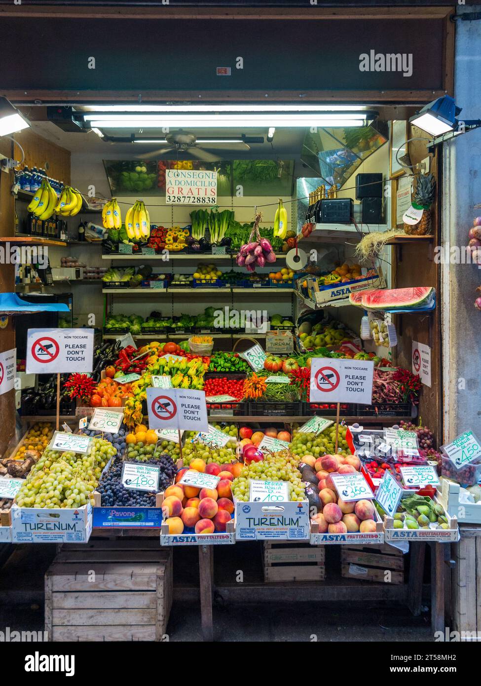 Un'esposizione di frutta e verdura da un mercante di Venezia. I cartelli indicano che non è necessario toccare la merce. L'interno del negozio è illuminato Foto Stock