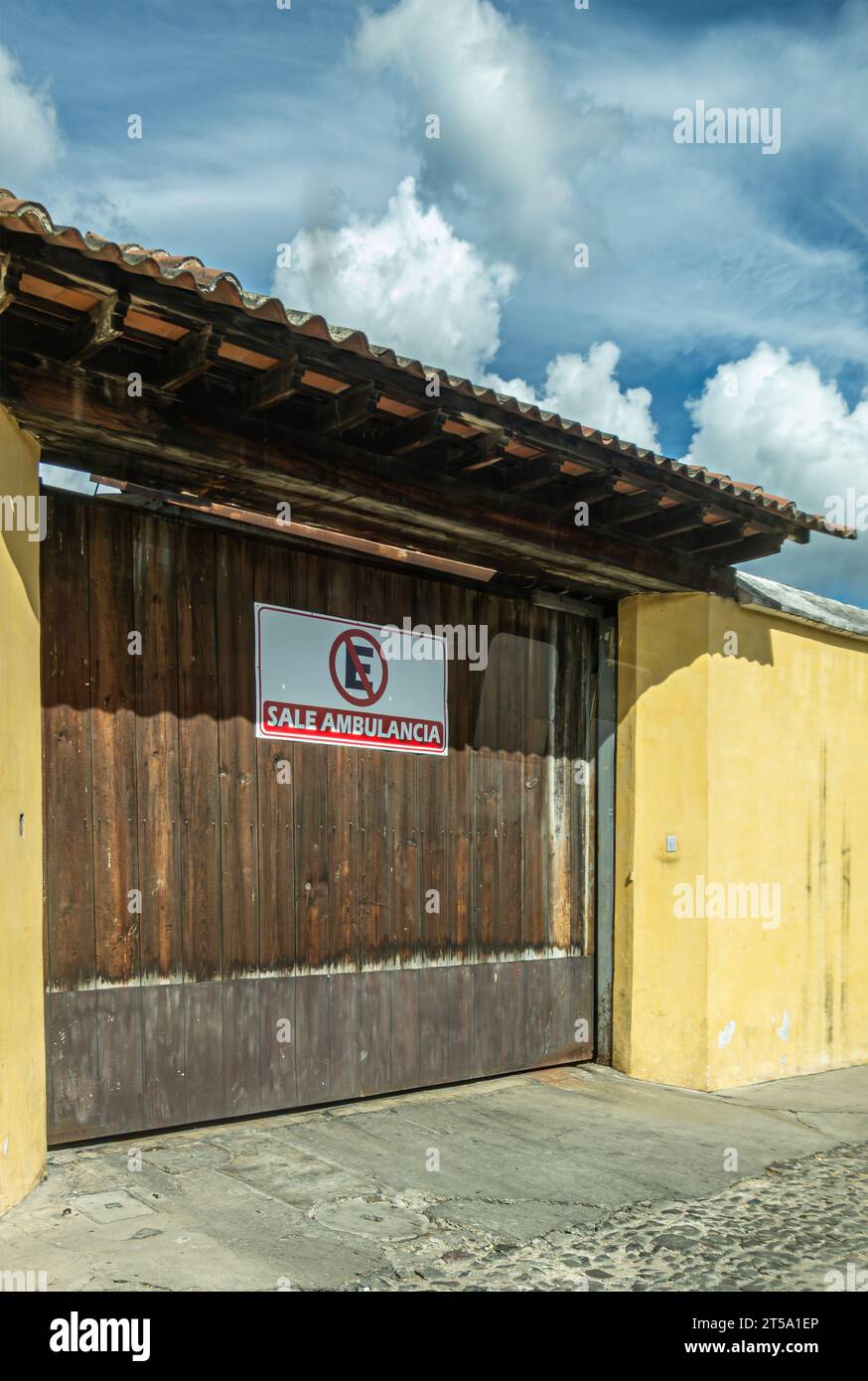 Guatemala, la Antigua - 20 luglio 2023: Il segnale di uscita dell'ambulanza sul cancello marrone proibisce il parcheggio davanti. Incastonata in parete gialla sotto il paesaggio blu, S Foto Stock