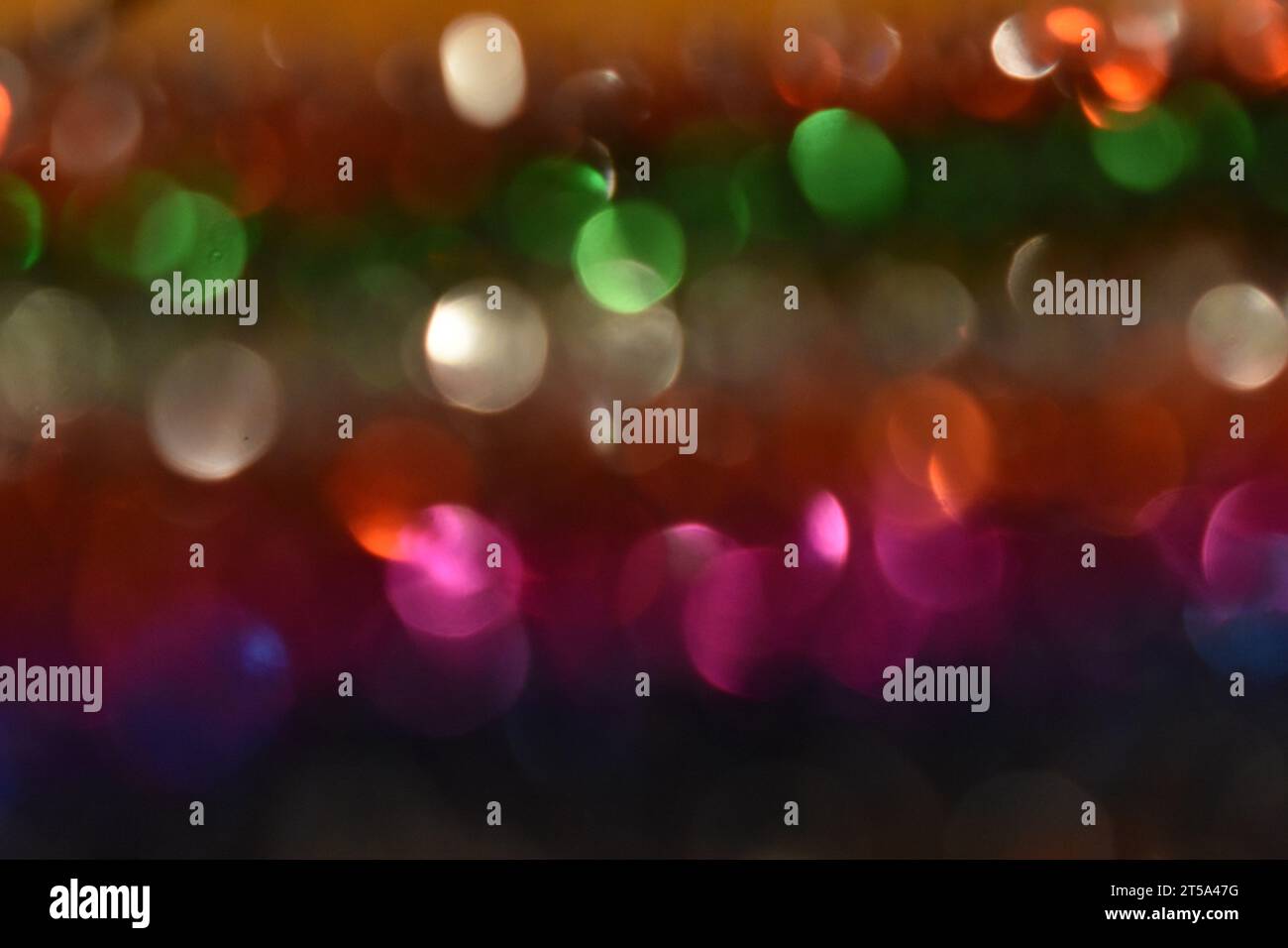 La luce si riflette su file di tinsel dai colori vivaci, creando un design bokeh astratto. Foto Stock