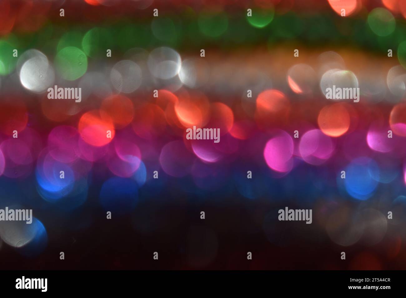La luce si riflette su file di tinsel dai colori vivaci, creando un design bokeh astratto. Foto Stock