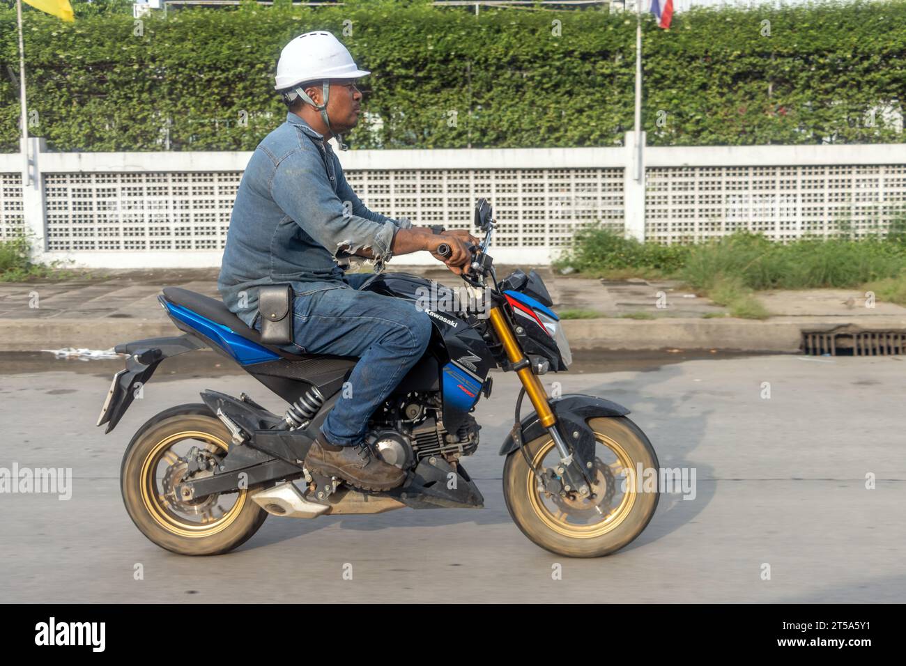SAMUT PRAKAN, THAILANDIA, ottobre 29 2023, Un uomo con un casco da lavoro guida una motocicletta Foto Stock
