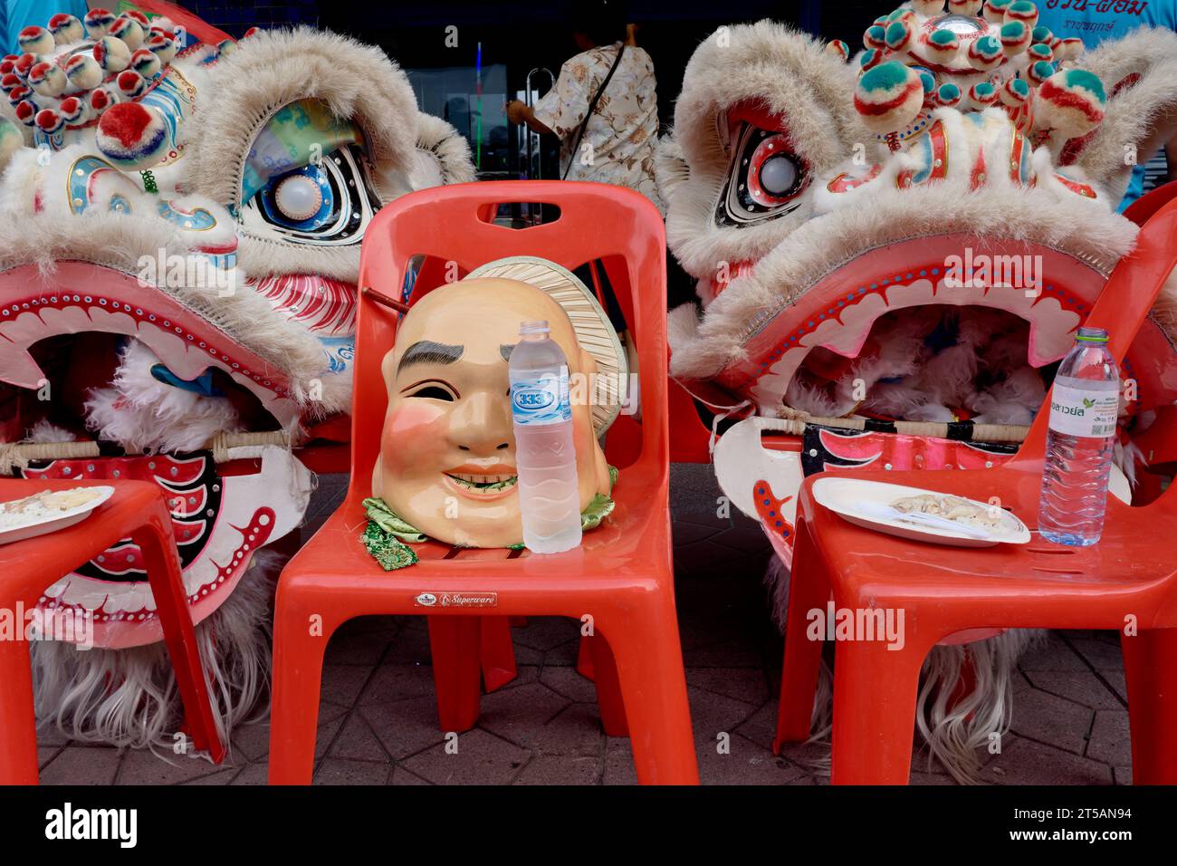 Dopo una festa taoista a Bangkok, in Thailandia, i membri di una compagnia di danza drago hanno scartato i loro abiti da drago e una maschera cinese sulle sedie rosse Foto Stock