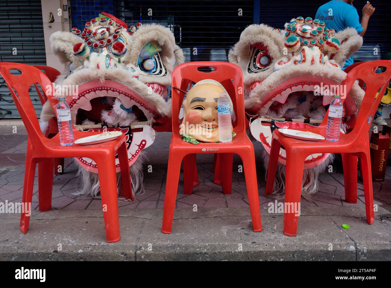 Dopo una festa taoista a Bangkok, in Thailandia, i membri di una compagnia di danza drago hanno scartato i loro abiti da drago e una maschera cinese sulle sedie rosse Foto Stock
