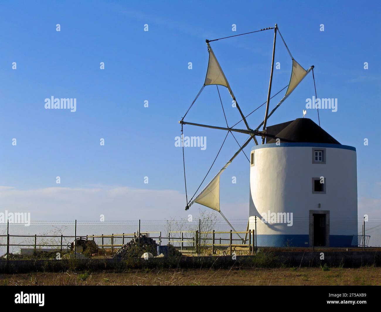 Tipico mulino a vento portoghese proveniente dalle regioni centrali e meridionali di Sesimbra, Portogallo. Vista delle vele di stoffa parzialmente srotolate dai montanti. Foto Stock