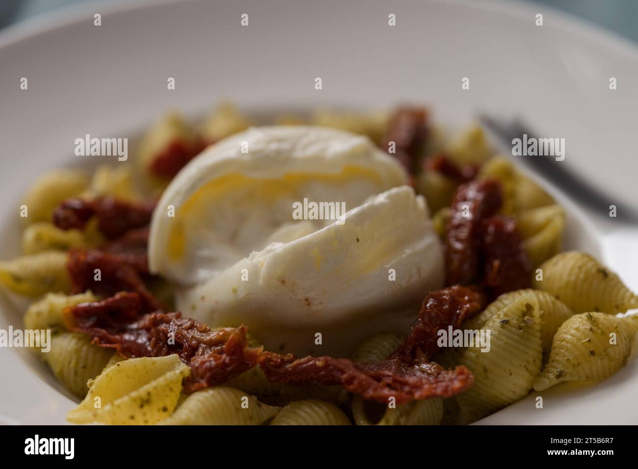 Primo piano di pesto conchiglie con pomodori secchi e burrata serviti in piatto bianco, poco profondo Foto Stock