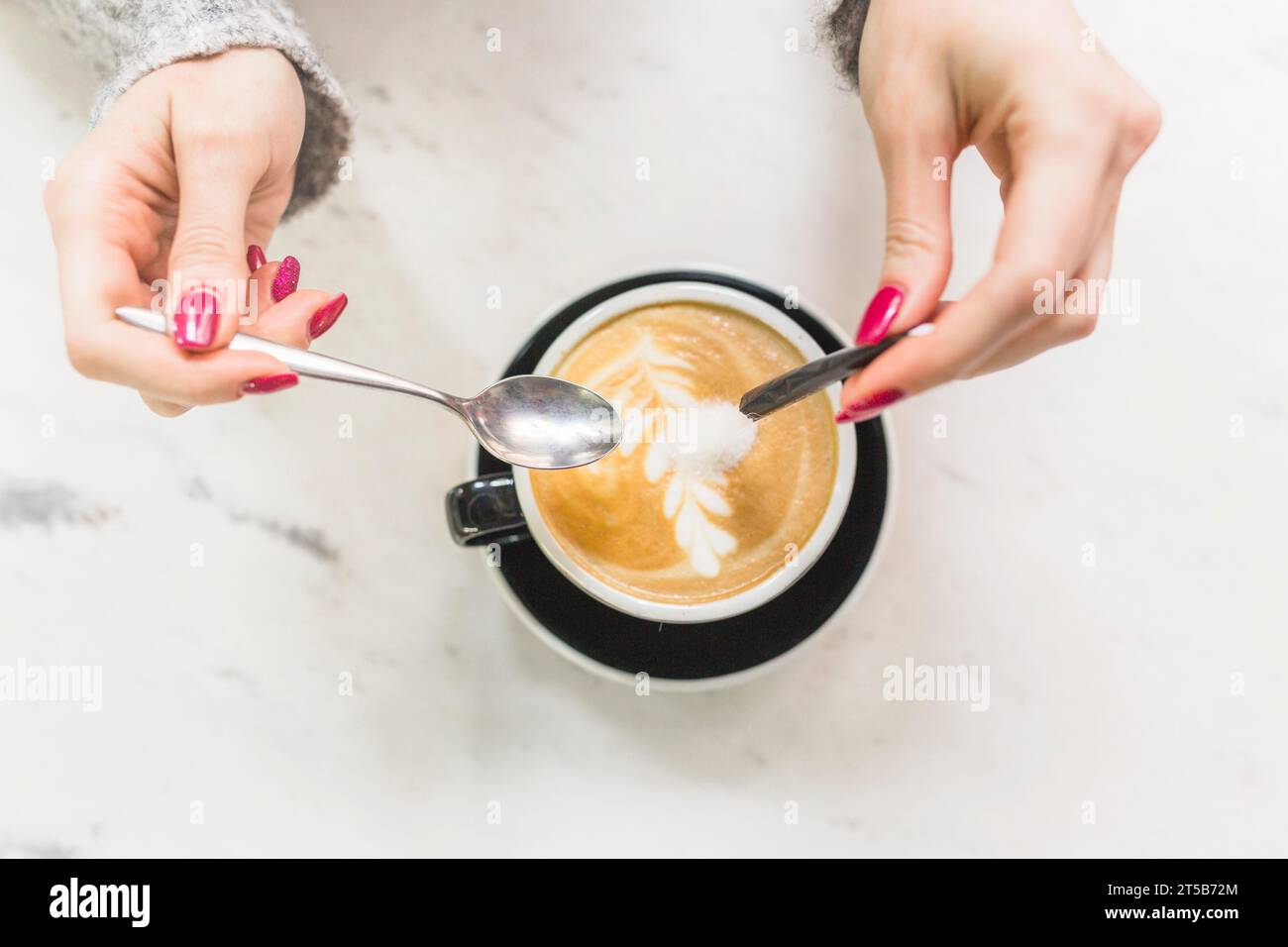 Tagliare le mani versando lo zucchero nella tazza per cappuccino Foto Stock