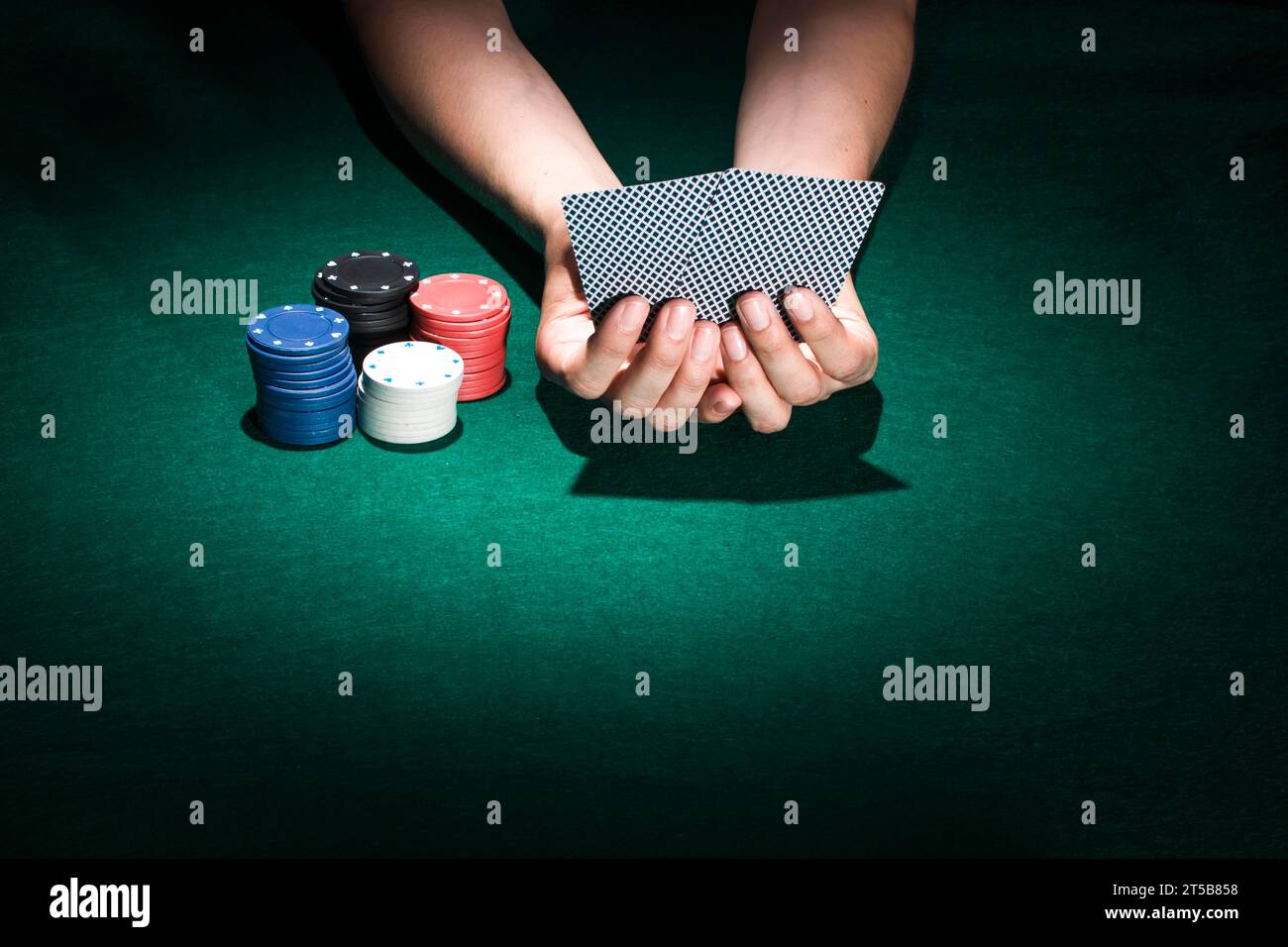 Persona che tiene la mano della carta da gioco con il tavolo del casinò con gettoni da poker impilabili Foto Stock