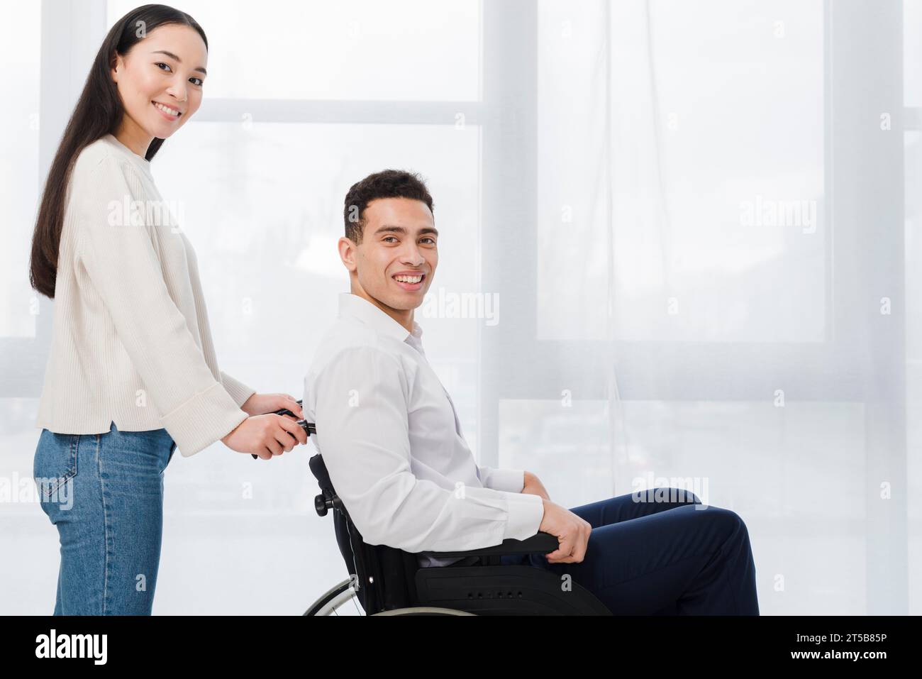 Ritratto giovane donna sorridente uomo in piedi seduto in sedia a rotelle che guarda la fotocamera Foto Stock