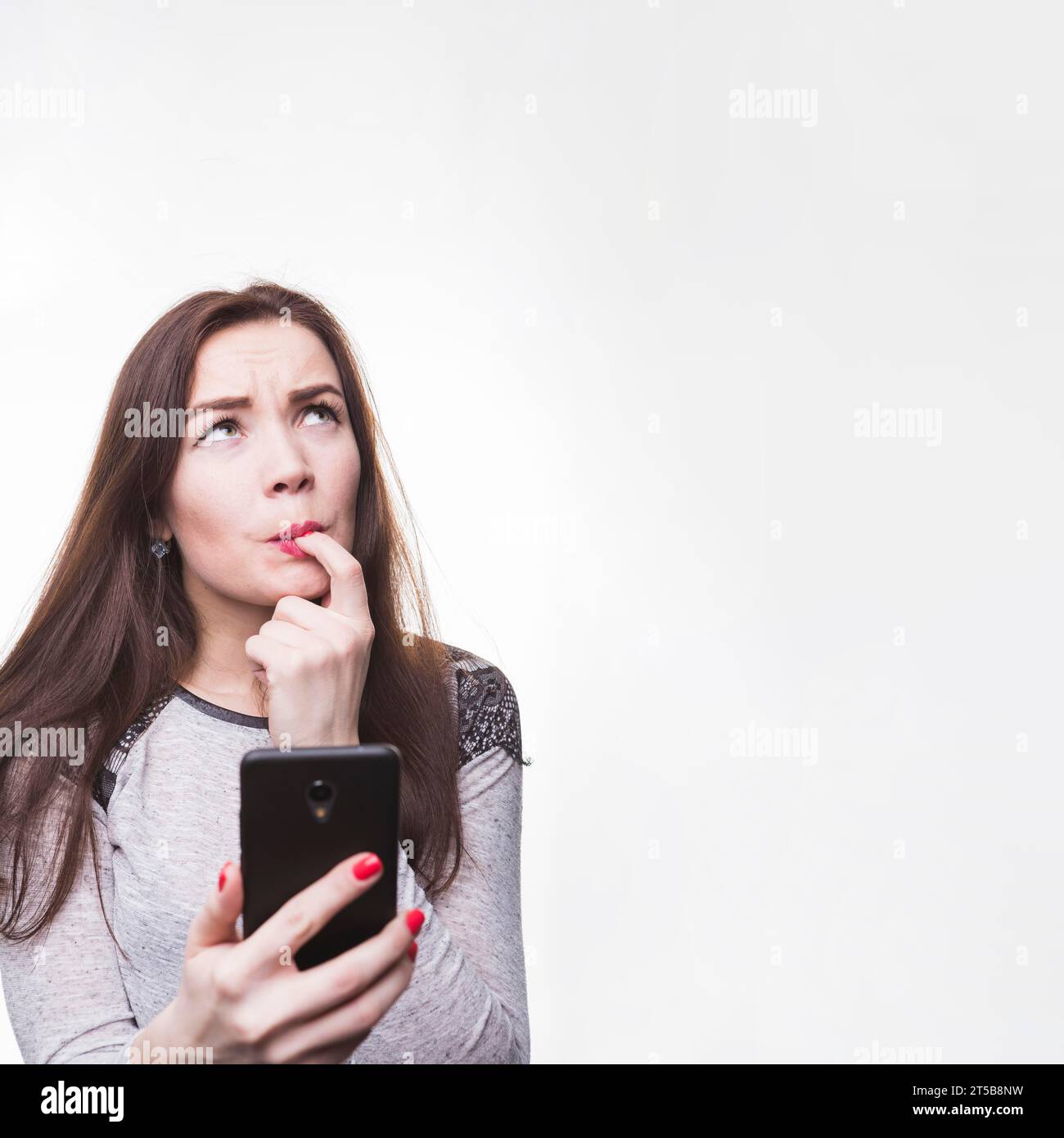 Giovane donna premurosa che tiene il telefono cellulare con le dita della bocca Foto Stock