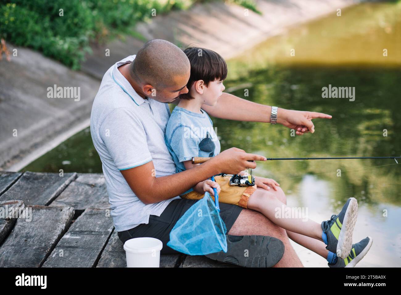 Fisherman mostra qualcosa a suo figlio mentre pesca il lago Foto Stock