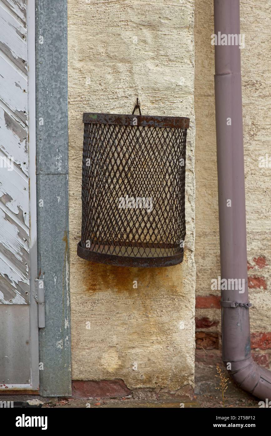 Primo piano del vecchio cestino per rifiuti metallici vuoto appeso a una parete di pietra gialla. Foto Stock