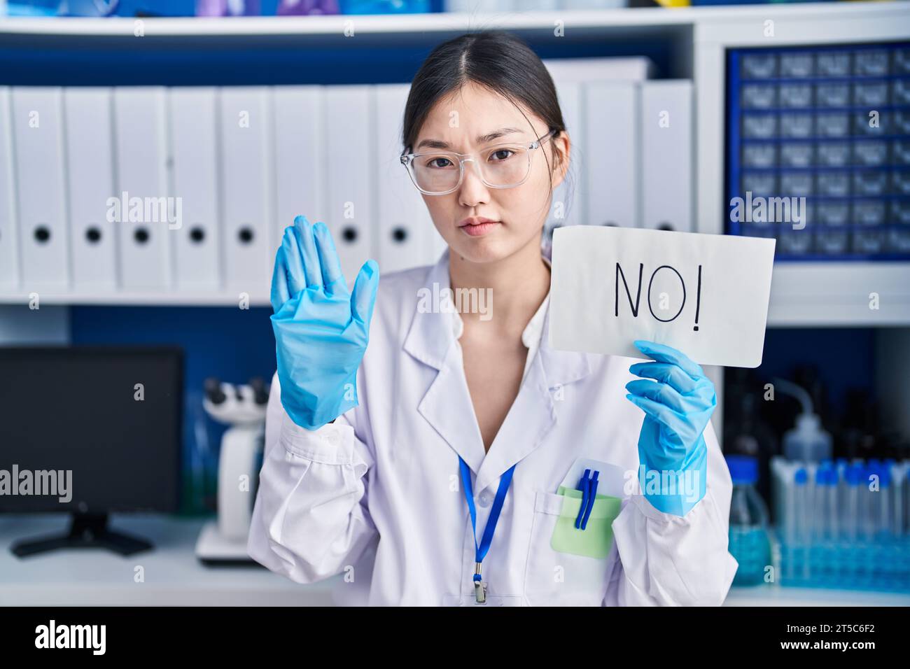 Giovane donna cinese che lavora in un laboratorio di scienziati senza striscioni a mano aperta, che fa stop sign con espressione seria e sicura, difesa ge Foto Stock