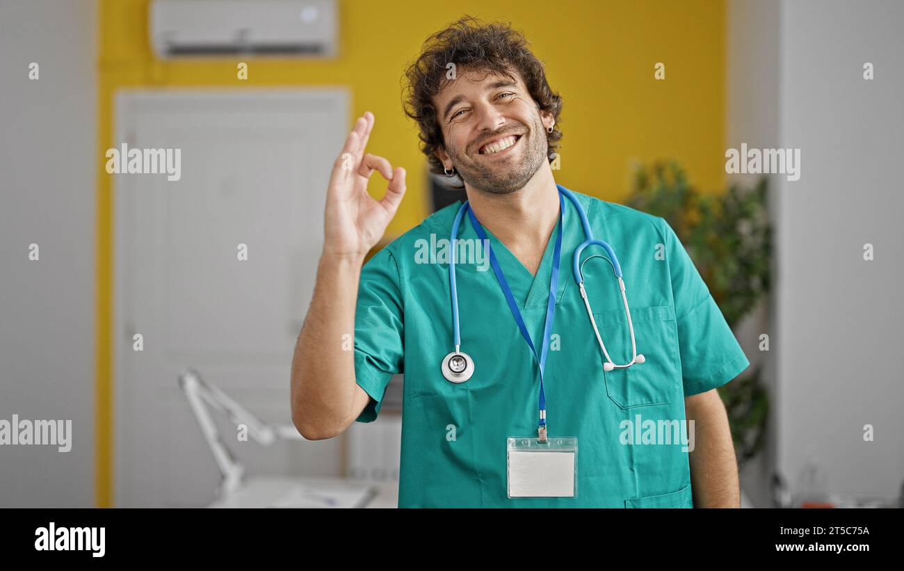 Giovane medico ispanico che fa un gesto ok sorridendo in clinica Foto Stock