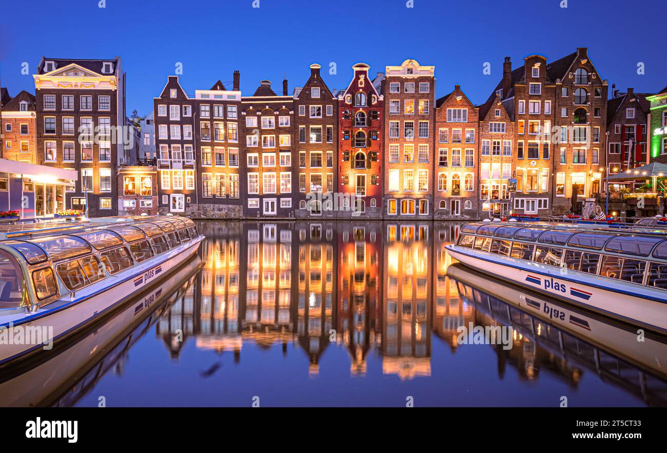 The Dancing Houses Damrak Amsterdam di notte con barche e riflesso di case nell'acqua Paesi Bassi Olanda Foto Stock