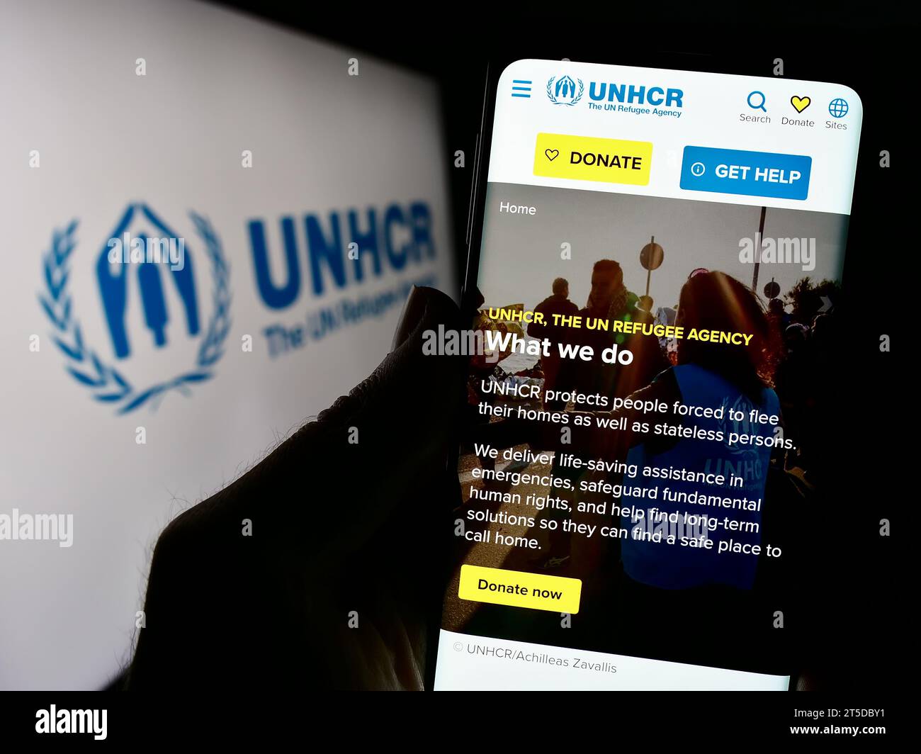 Persona in possesso di cellulare con pagina web dell'alto Commissariato delle Nazioni Unite per i rifugiati (UNHCR) davanti al logo. Concentrarsi sul centro del display del telefono. Foto Stock