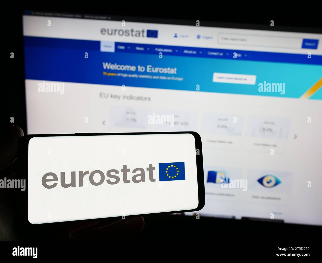 Persona in possesso di uno smartphone con il logo dell'Istituto europeo di statistica Eurostat di fronte al sito web. Concentrarsi sul display del telefono. Foto Stock