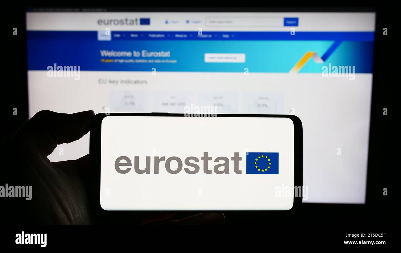 Persona in possesso di un cellulare con il logo dell'Istituto europeo di statistica Eurostat davanti alla pagina web delle imprese. Concentrarsi sul display del telefono. Foto Stock