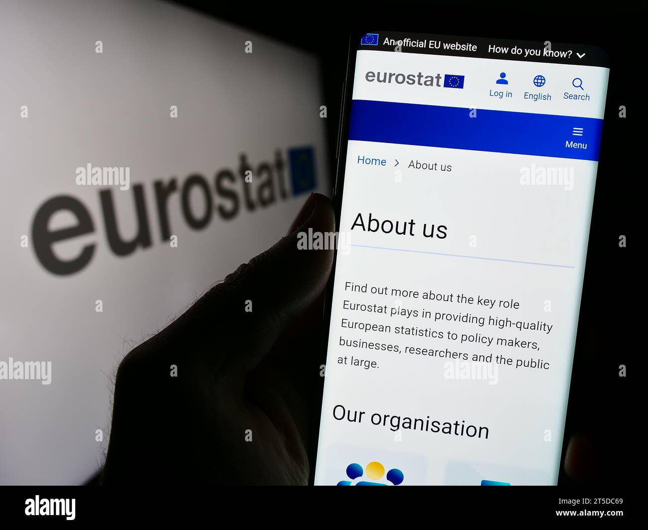 Persona in possesso di smartphone con pagina web dell'Istituto europeo di statistica Eurostat davanti al logo. Concentrarsi sul centro del display del telefono. Foto Stock