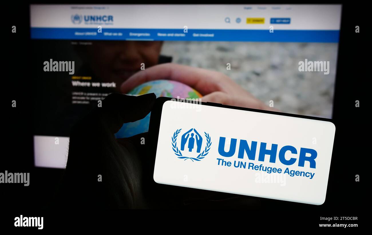 Persona in possesso di un telefono cellulare con il logo dell'alto Commissariato delle Nazioni Unite per i rifugiati (UNHCR) davanti alla pagina web. Concentrarsi sul display del telefono. Foto Stock