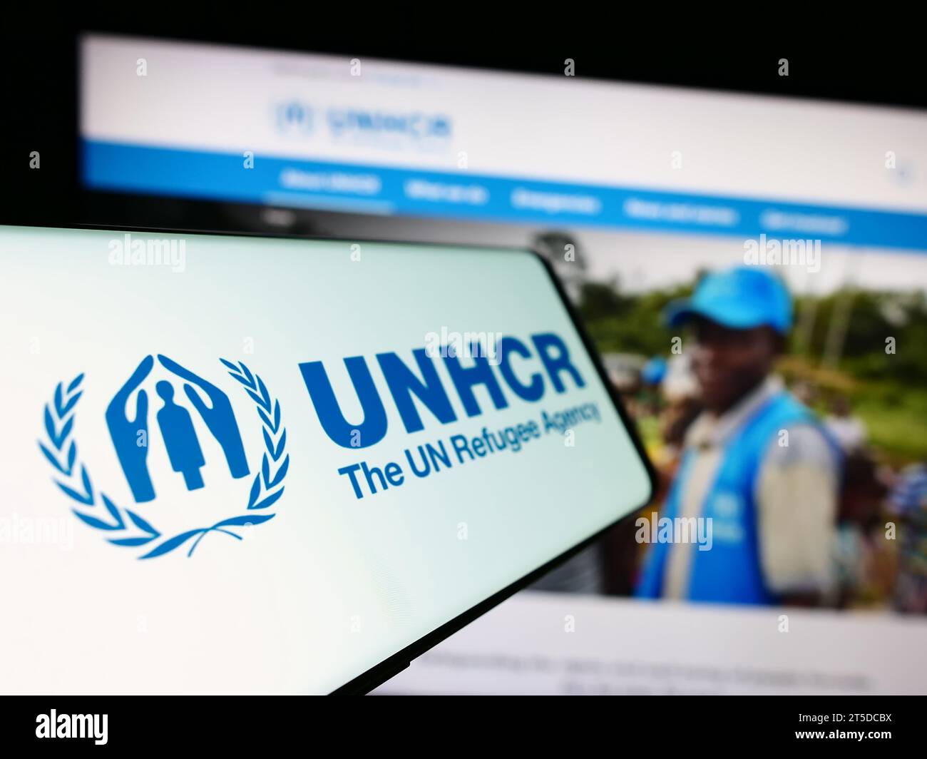 Smartphone con logo dell'alto Commissariato delle Nazioni Unite per i rifugiati (UNHCR) davanti al sito web. Mettere a fuoco il display centrale sinistro del telefono. Foto Stock