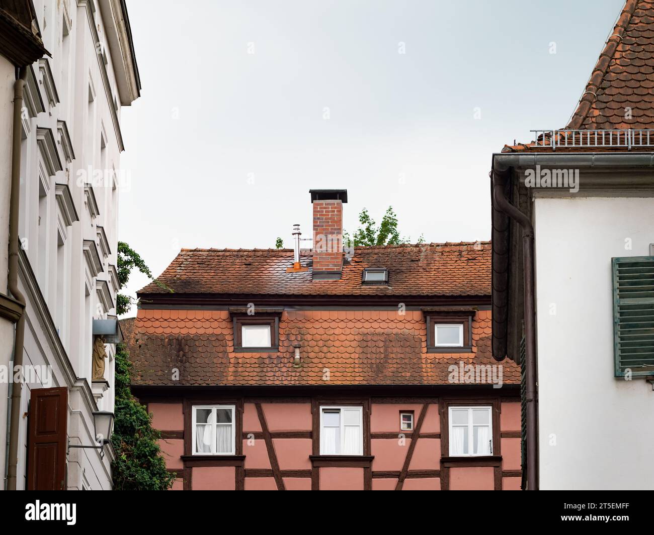 Edificio in legno per metà esterno in una città. Il tetto e l'esterno sono contaminati e sporchi. La vecchia casa fa parte di un quartiere residenziale. Foto Stock