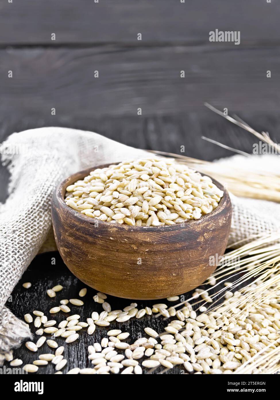 Scritto in una ciotola e sul tavolo, steli con orecchie di grano, un tovagliolo da rapa sullo sfondo di una tavola di legno nera Foto Stock