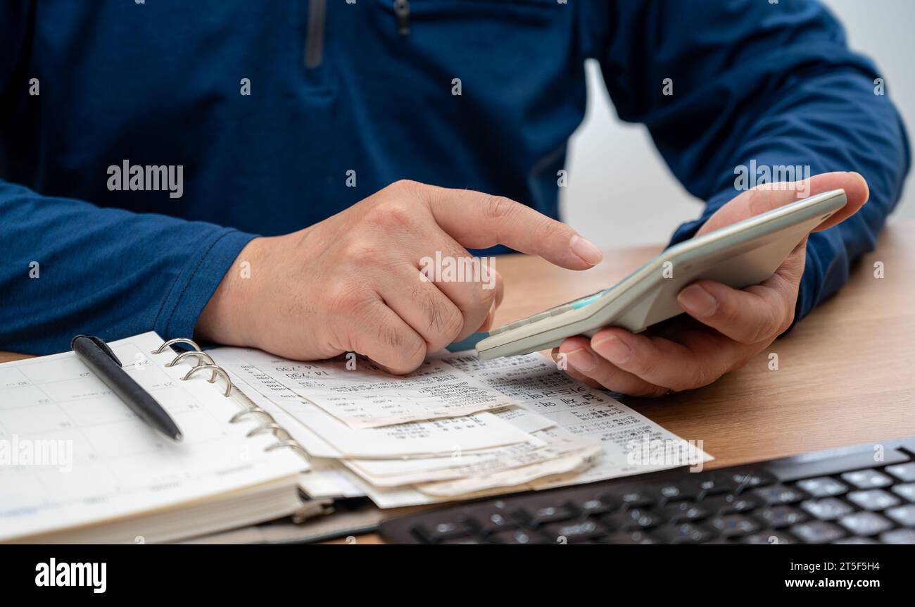 Un uomo sta scrivendo un registro di famiglia mentre organizza le ricevute. Un primo piano di mani. Concetto di liquidazione fiscale o di fine anno. Foto Stock