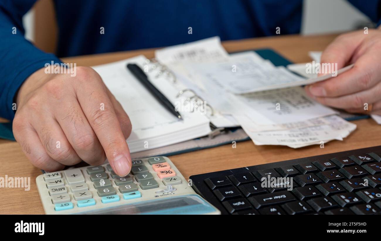 Un uomo sta scrivendo un registro di famiglia mentre organizza le ricevute. Un primo piano di mani. Concetto di liquidazione fiscale o di fine anno. Foto Stock