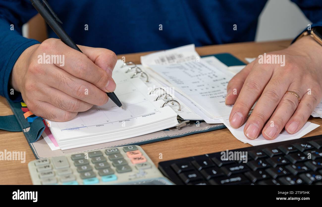 Un uomo sta scrivendo un registro di famiglia mentre organizza le ricevute. Un primo piano di mani. Concetto di liquidazione fiscale o di fine anno. Foto Stock