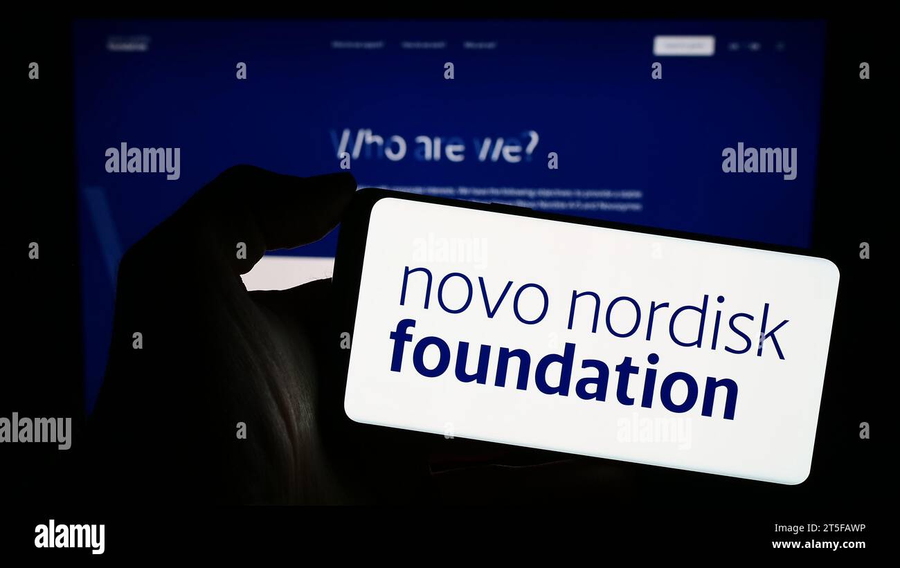 Persona che possiede un telefono cellulare con il logo dell'organizzazione danese Novo Nordisk Foundation davanti alla pagina Web. Concentrarsi sul display del telefono. Foto Stock