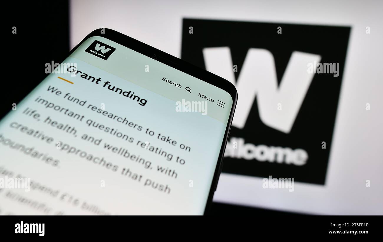 Smartphone con pagina Web della fondazione benefica britannica Wellcome Trust davanti al logo. Mettere a fuoco in alto a sinistra sul display del telefono. Foto Stock