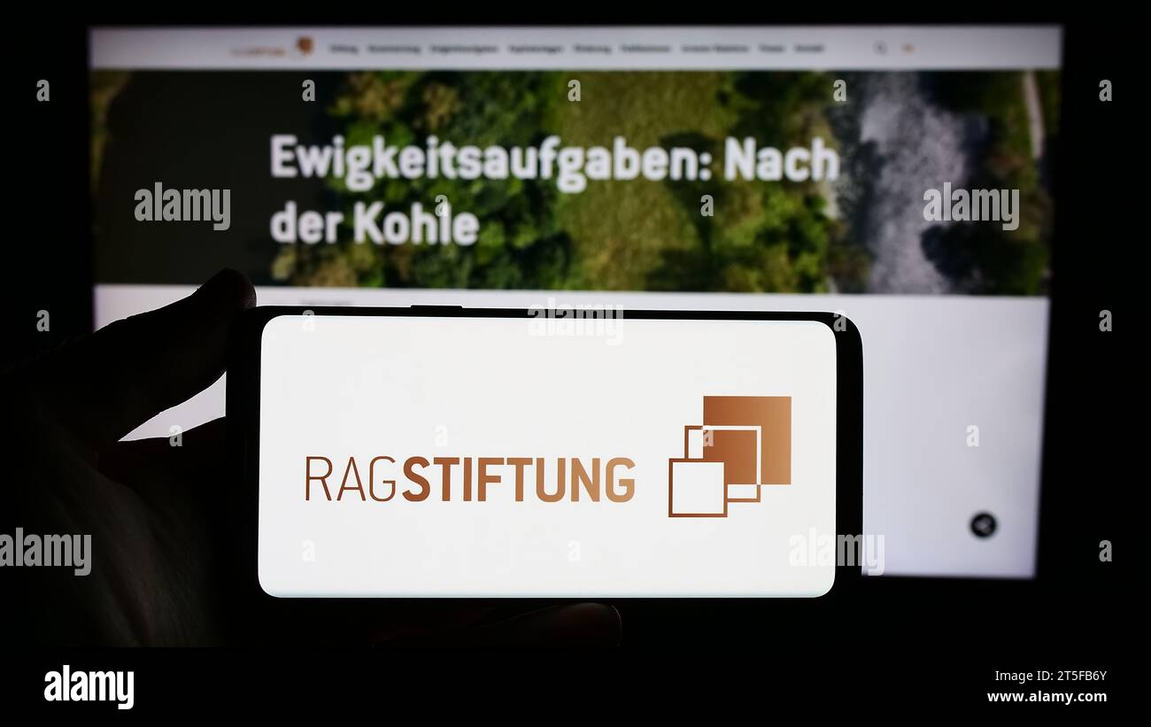 Persona che possiede uno smartphone con il logo della fondazione tedesca RAG-Stiftung davanti al sito Web. Concentrarsi sul display del telefono. Foto Stock