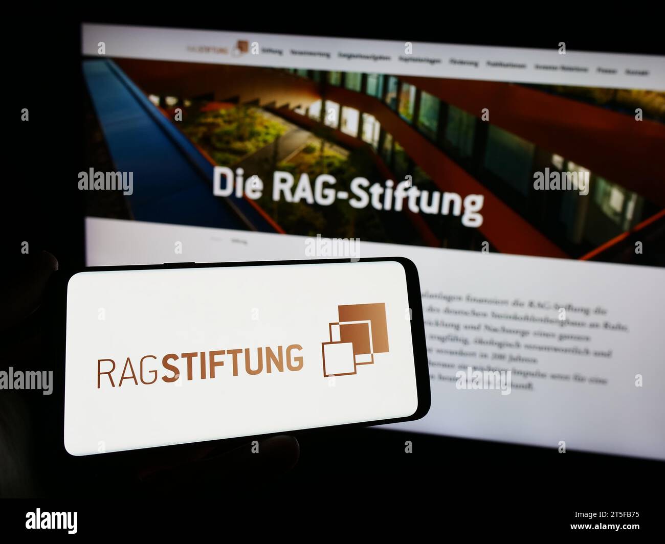 Persona che possiede un telefono cellulare con il logo della fondazione tedesca RAG-Stiftung davanti alla pagina web. Concentrarsi sul display del telefono. Foto Stock
