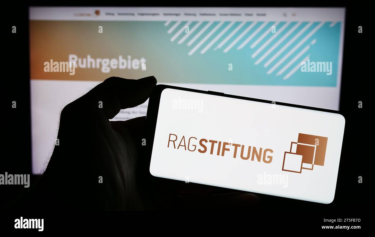 Persona che tiene il cellulare con il logo della fondazione tedesca RAG-Stiftung davanti alla pagina web. Concentrarsi sul display del telefono. Foto Stock