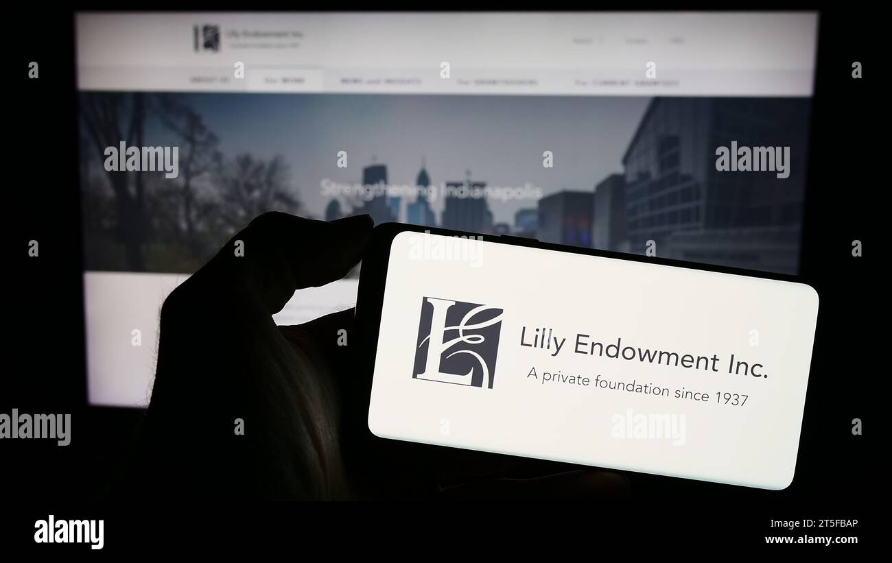 Persona che possiede un telefono cellulare con il logo della fondazione americana Lilly Endowment Inc. Davanti alla pagina Web. Concentrarsi sul display del telefono. Foto Stock