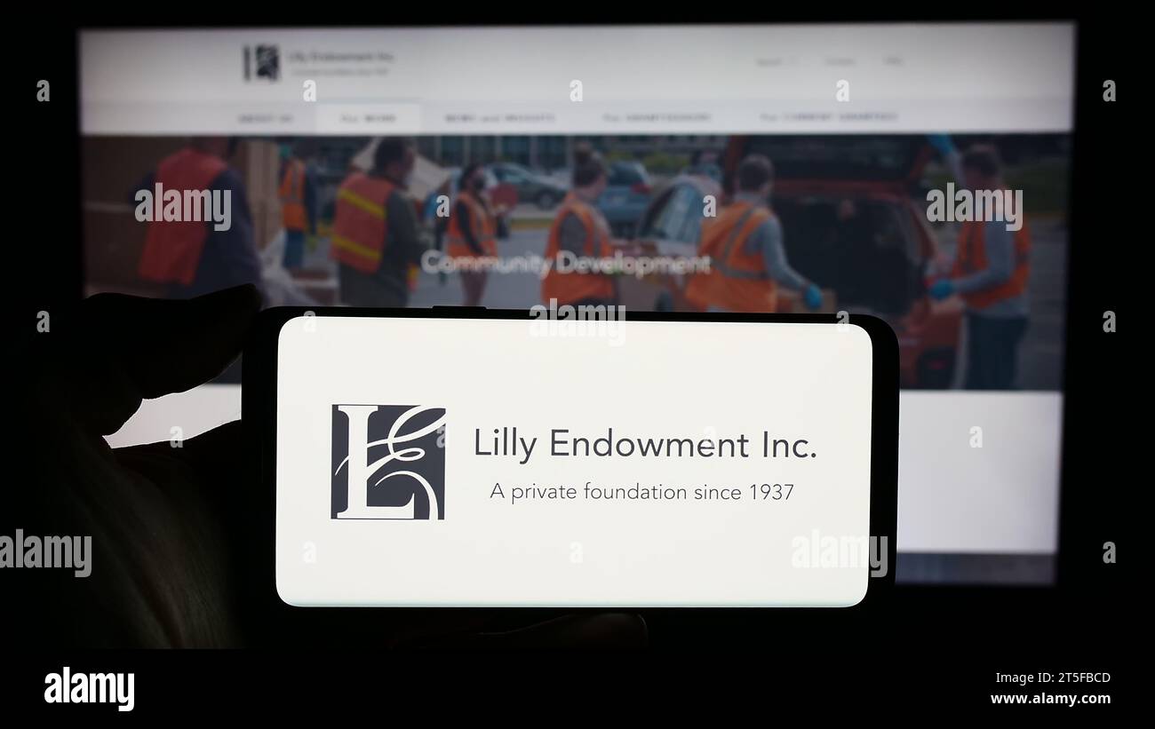 Persona che possiede il cellulare con il logo della fondazione statunitense Lilly Endowment Inc. Davanti alla pagina Web. Concentrarsi sul display del telefono. Foto Stock