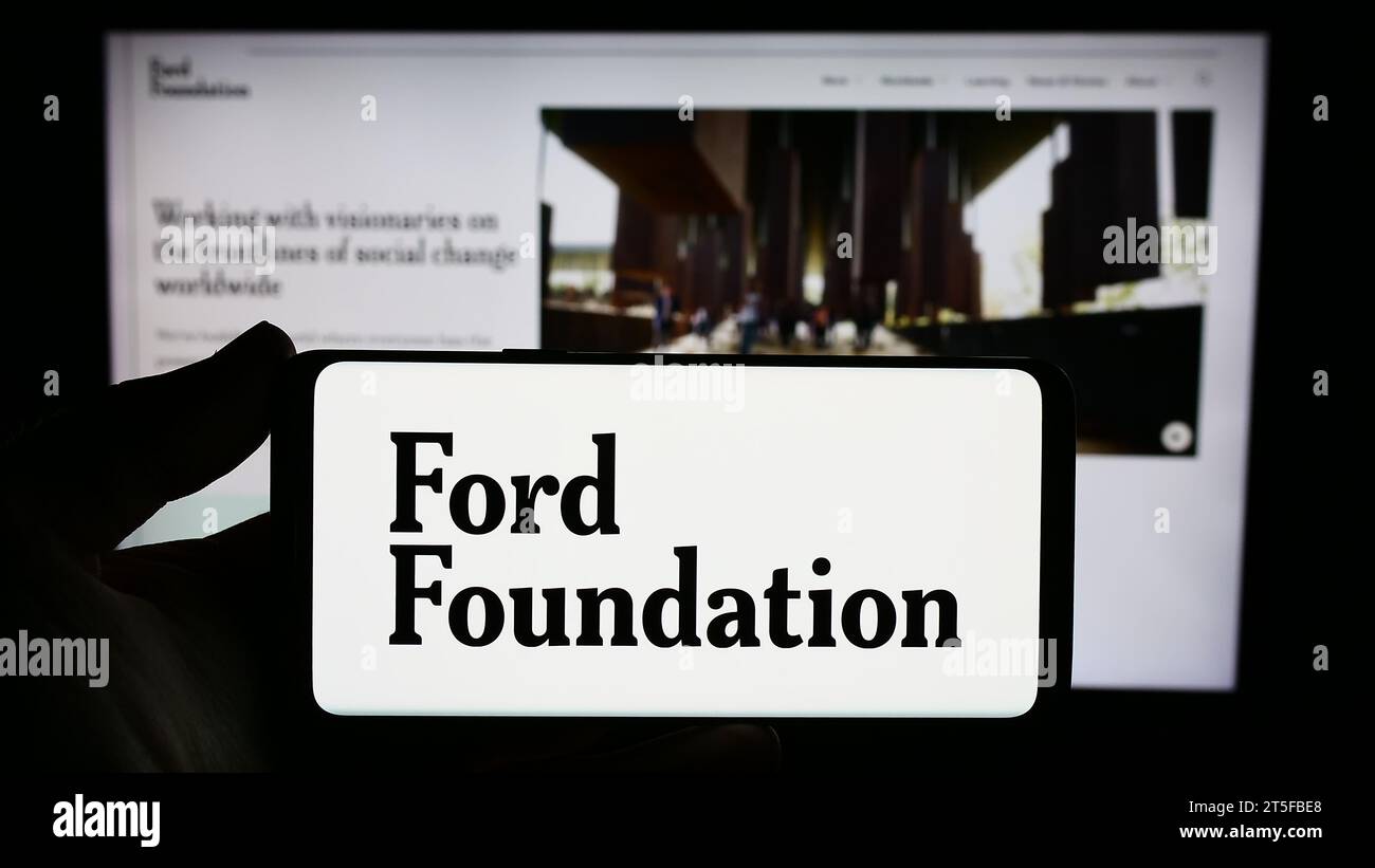 Persona che possiede uno smartphone con il logo dell'organizzazione di beneficenza statunitense Ford Foundation davanti al sito Web. Concentrarsi sul display del telefono. Foto Stock