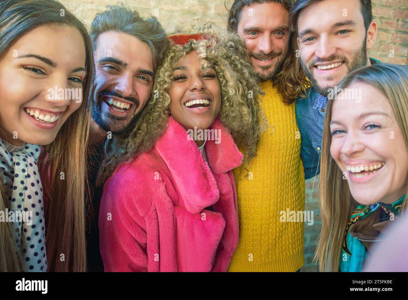 Un gruppo eterogeneo di amici che ridono e fanno un selfie, irradia gioia e amicizia in una strada urbana. Foto Stock