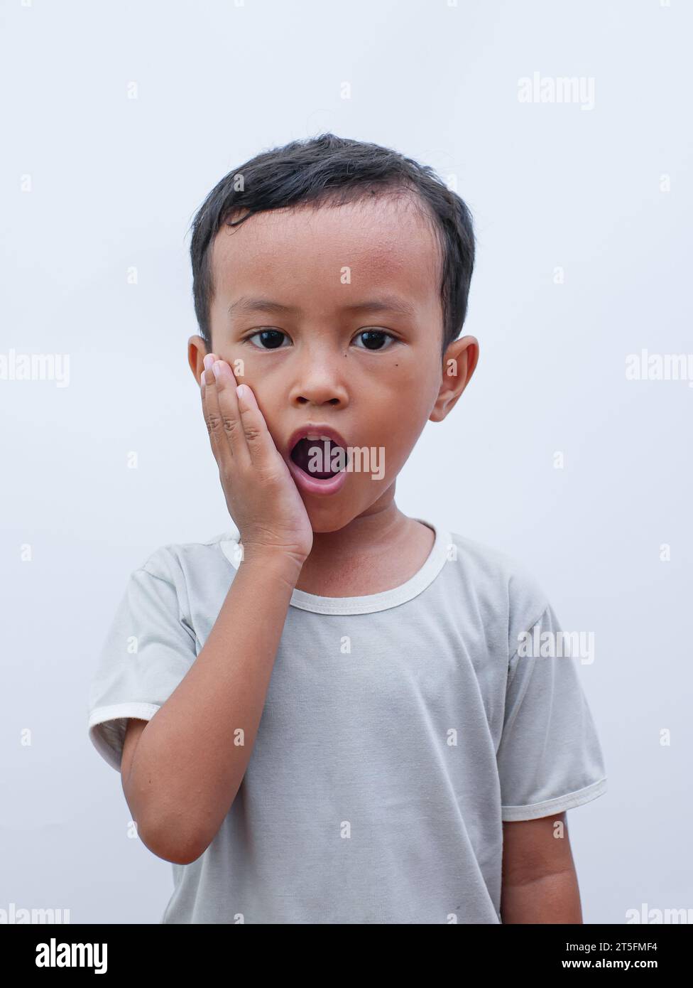 Ritratto di un ragazzino asiatico che tiene la guancia con mal di denti. soffre di mal di denti in bocca Foto Stock