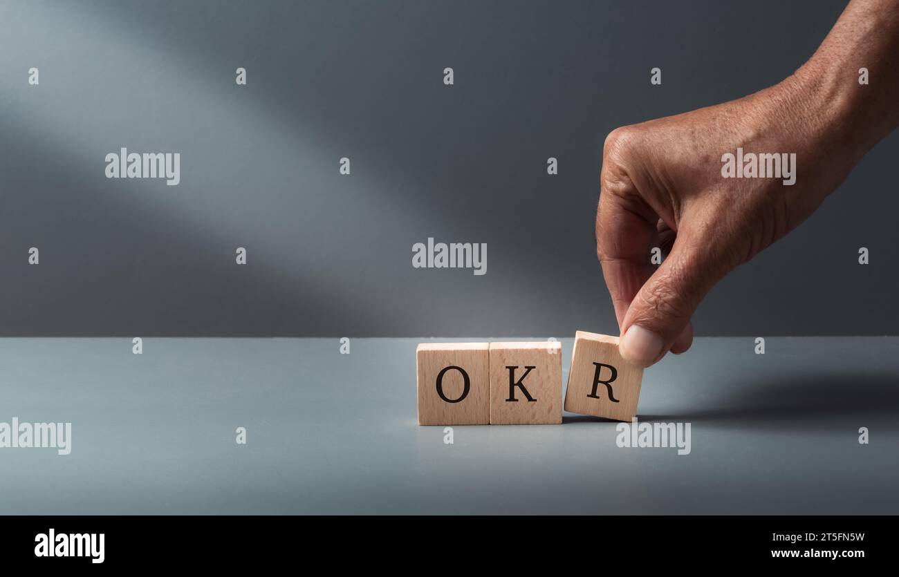OKR, obiettivi, chiave, risultati, mano con blocchi cubi in legno con testo OKR su sfondo grigio blu . Concetto di obiettivo aziendale e prestazioni. Foto Stock