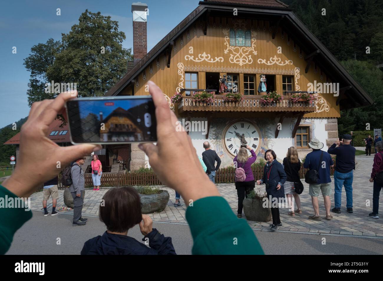 Breitnau, Baden-Würtenberg, Germania - agosto 30 2023: I turisti sorridenti scattano foto e selfie davanti a una facciata con un gigantesco orologio a cucù Foto Stock
