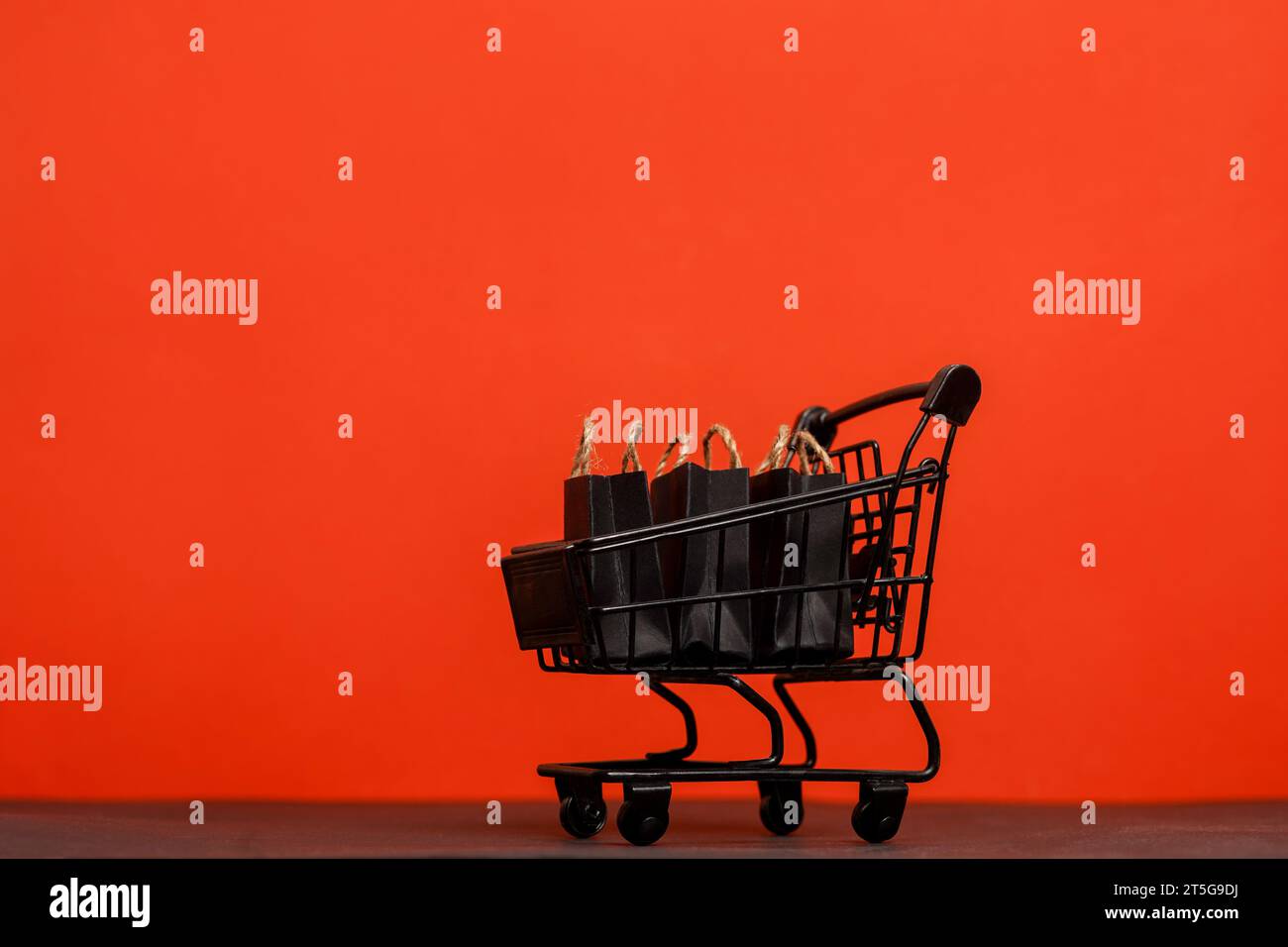 Carrello nero con sacchetti di carta su sfondo rosso, spazio per le copie. black friday Foto Stock